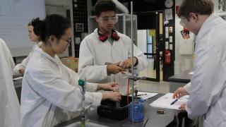 Three IB students perform a chemistry experiment in chemistry class.